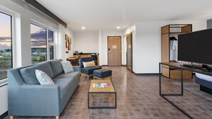 A modern living room with a sofa, ottoman, coffee table, and a TV. There is a wooden cabinet and a door leading to another room. - Hotel Indigo Everett - Waterfront Place by IHG (Everett)