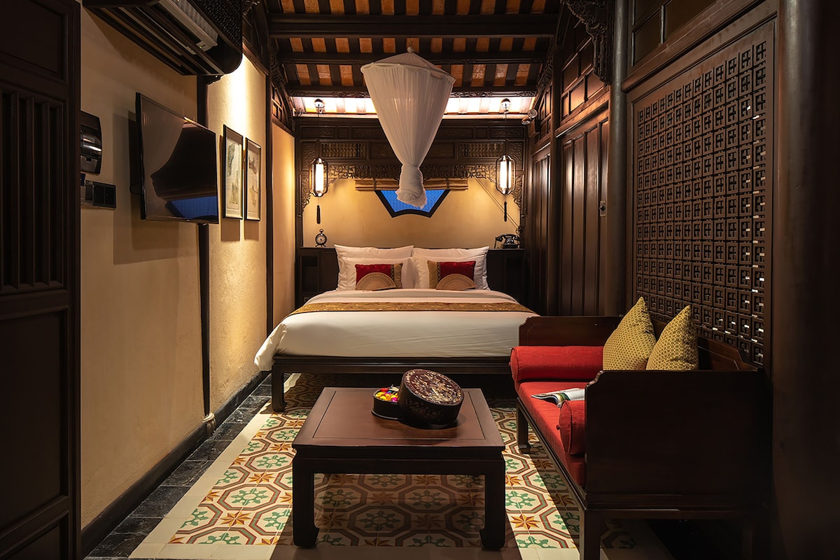 A hotel room with a large bed, a red sofa, a small table with a decorative item, and a patterned floor.