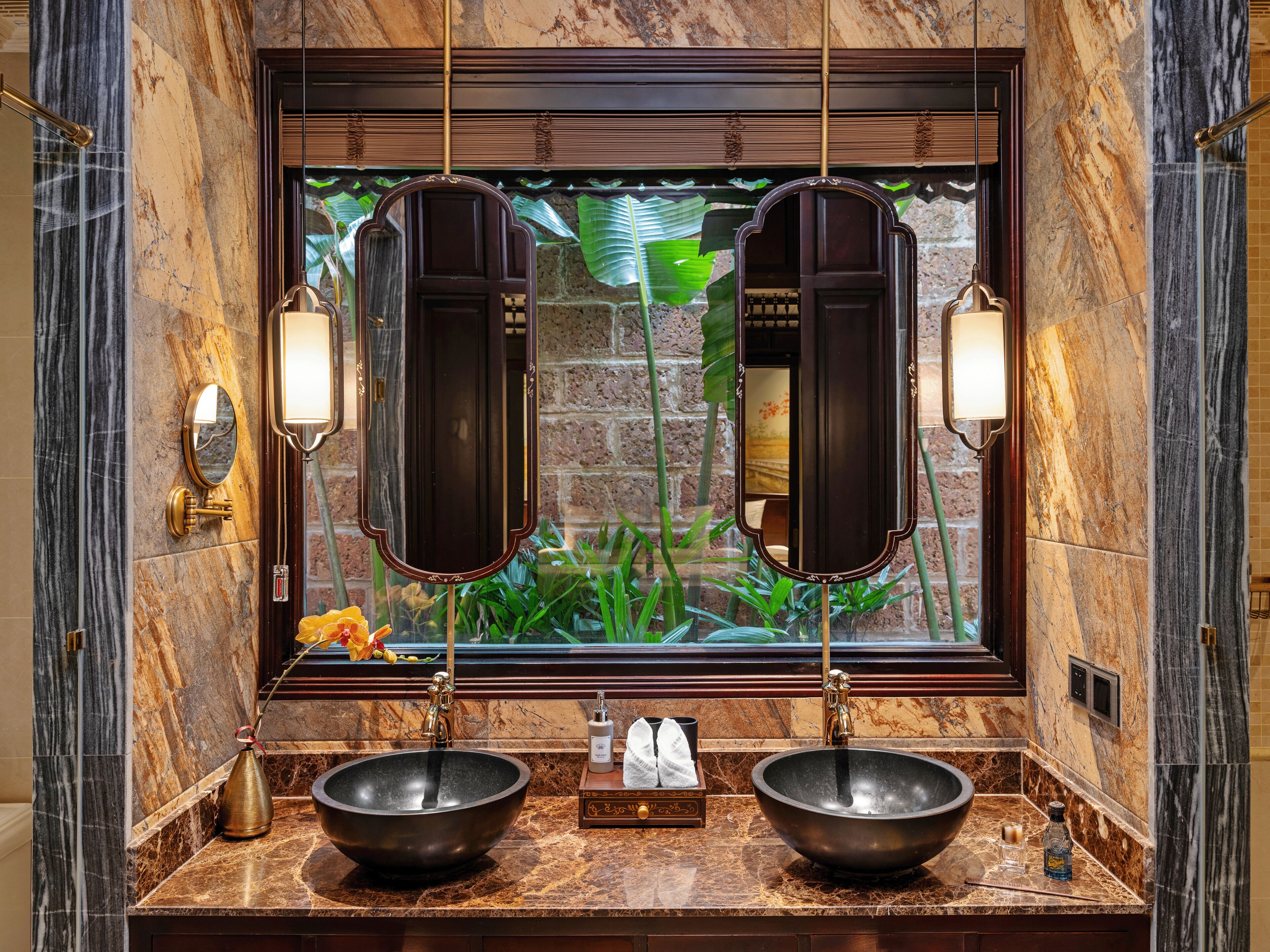 A bathroom with two large mirrors, a sink with a bowl, and a window with a view of greenery.