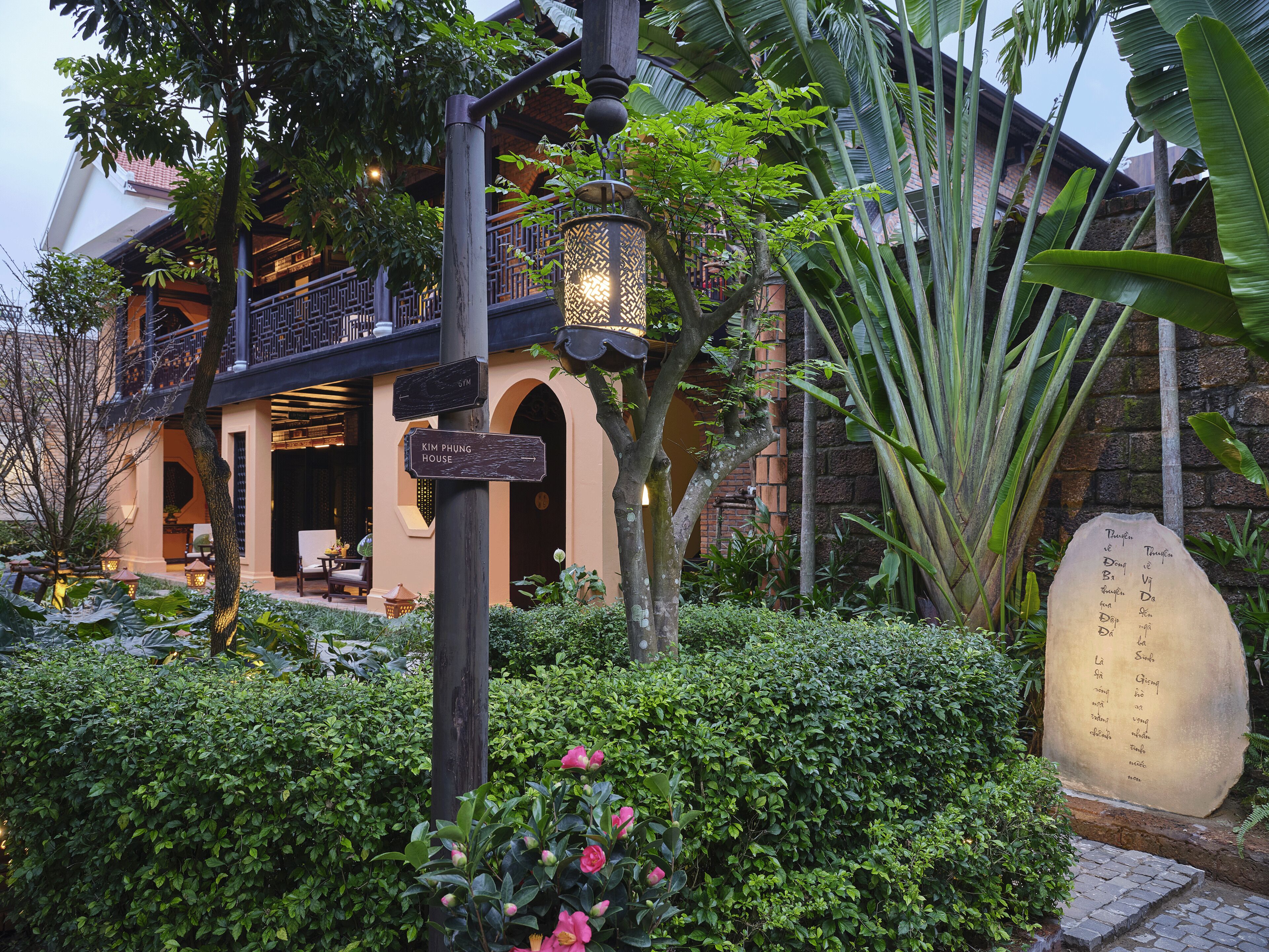 A traditional building with a balcony, surrounded by lush greenery and a stone plaque.