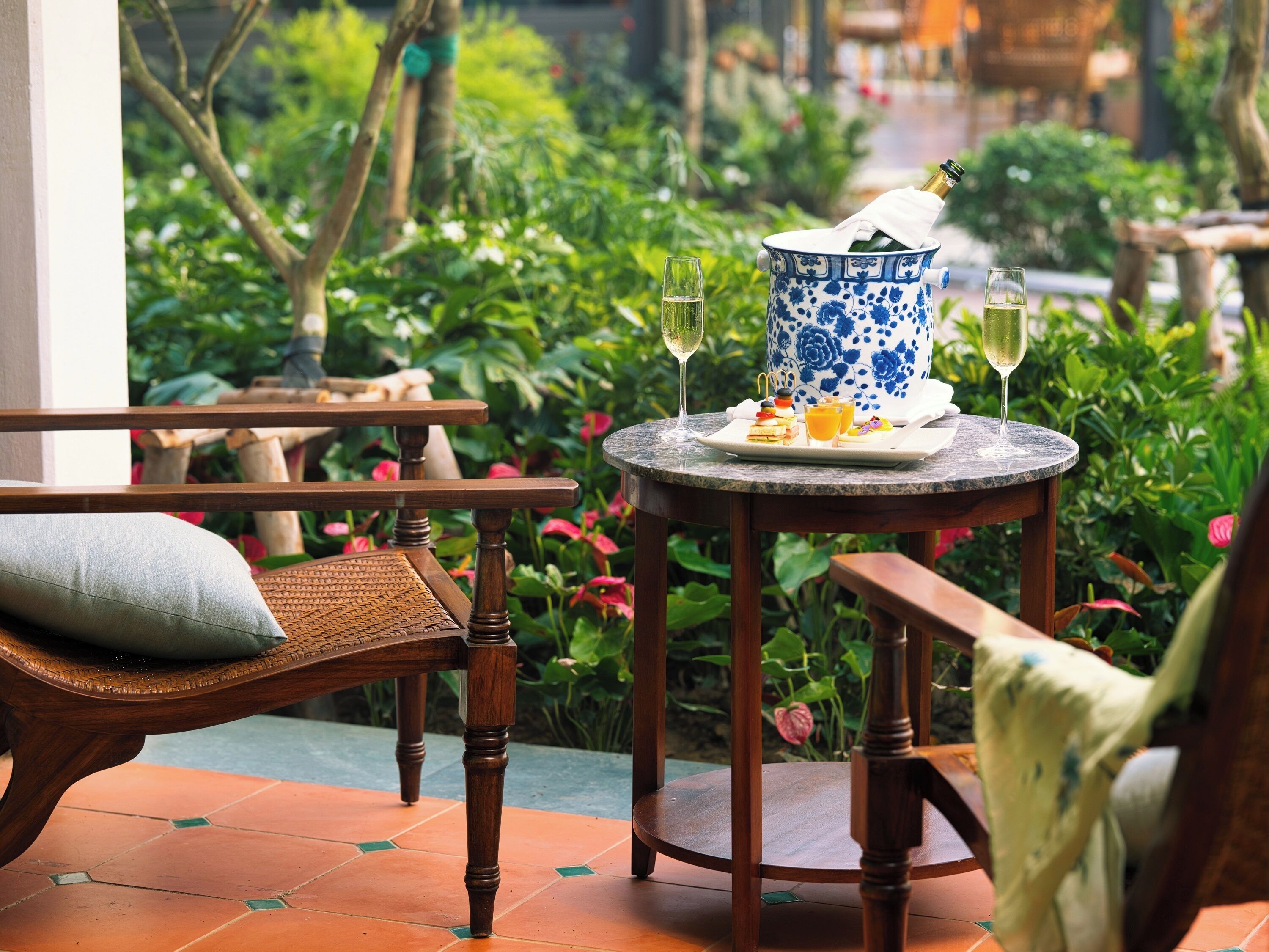 A round table with a blue and white floral vase, a bottle of champagne, and two glasses of wine.