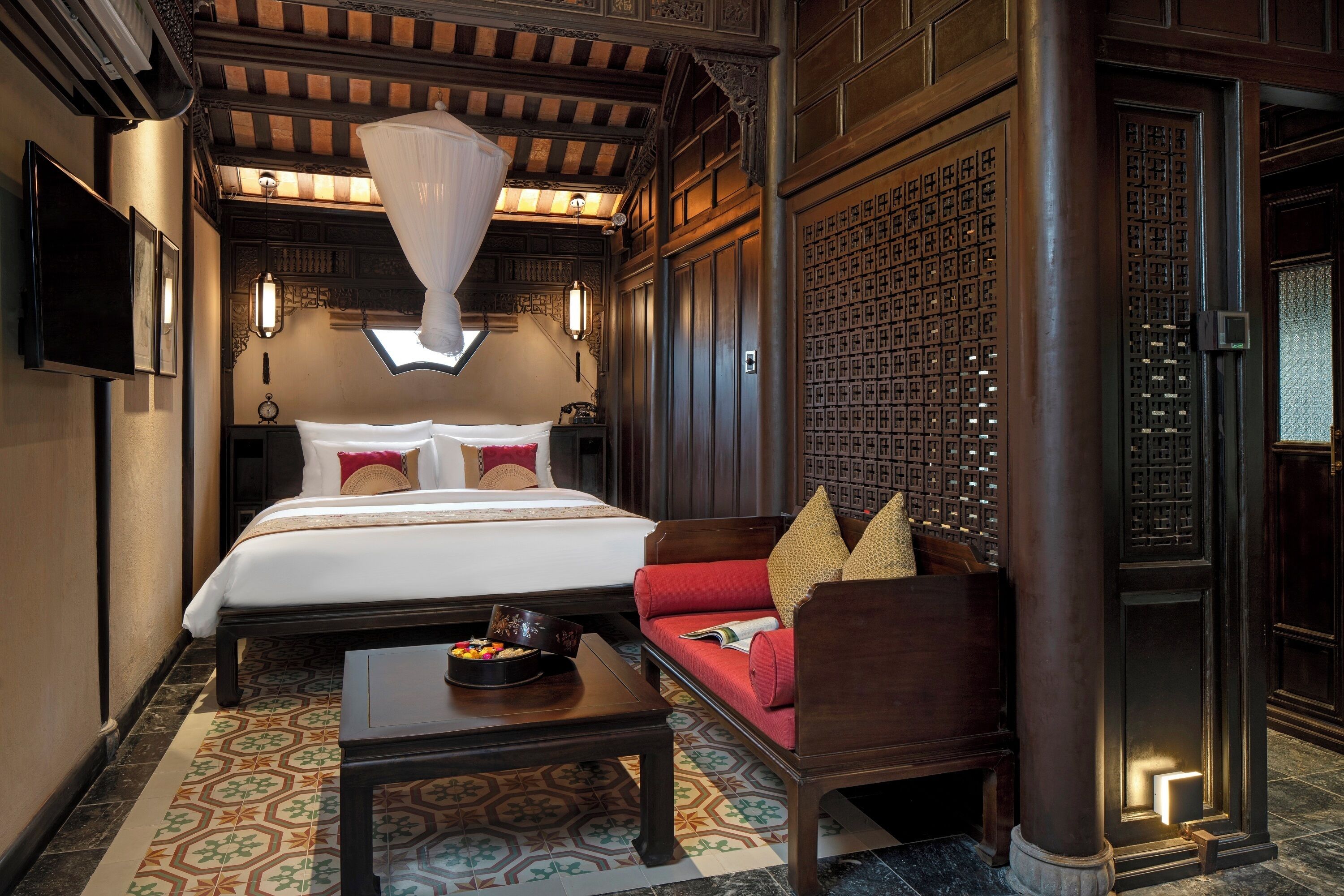 A traditional room with a bed, a sofa, a coffee table, and a decorative wall panel.