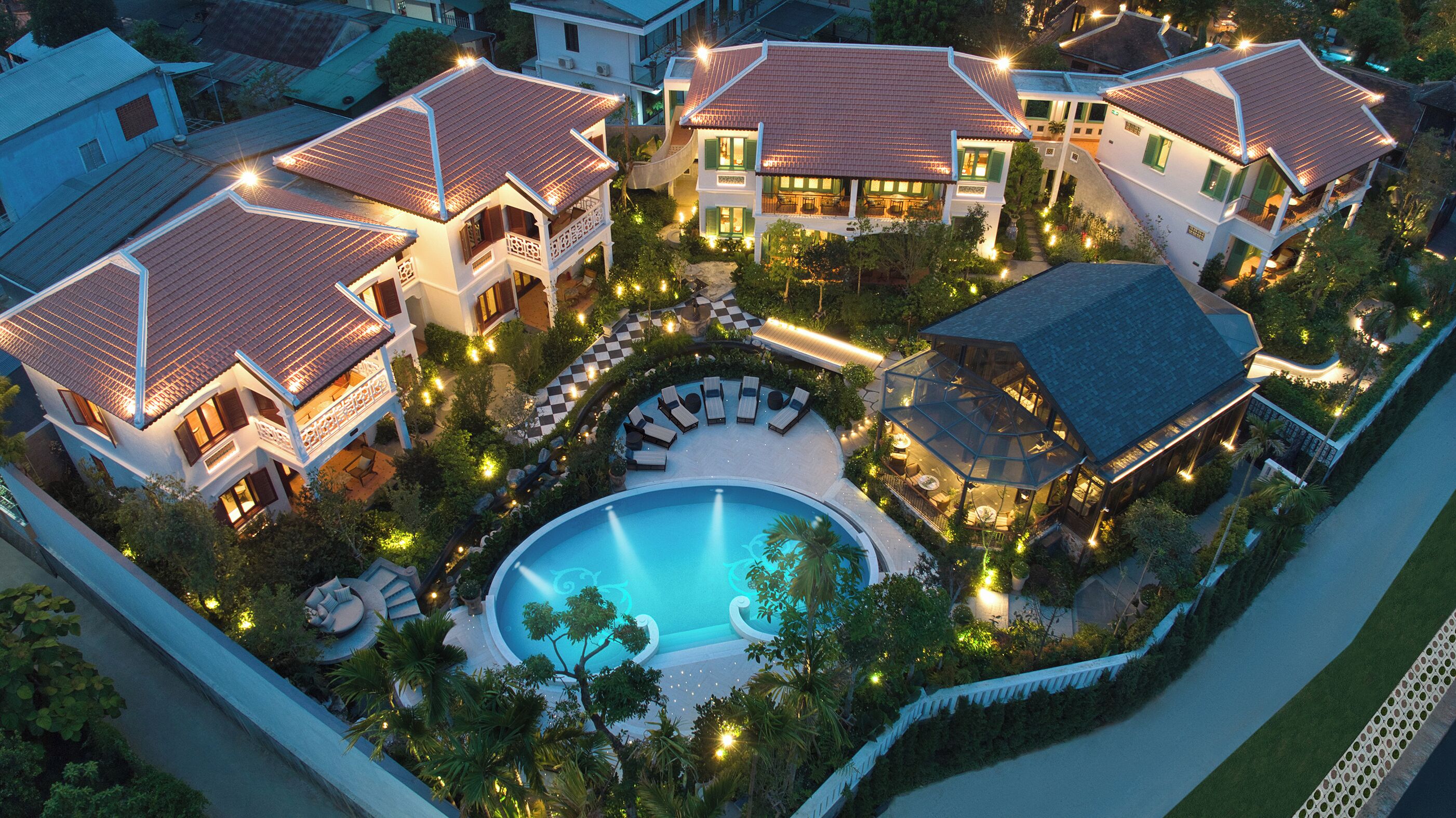 A luxurious resort with multiple villas, a central swimming pool, and well-lit outdoor areas.