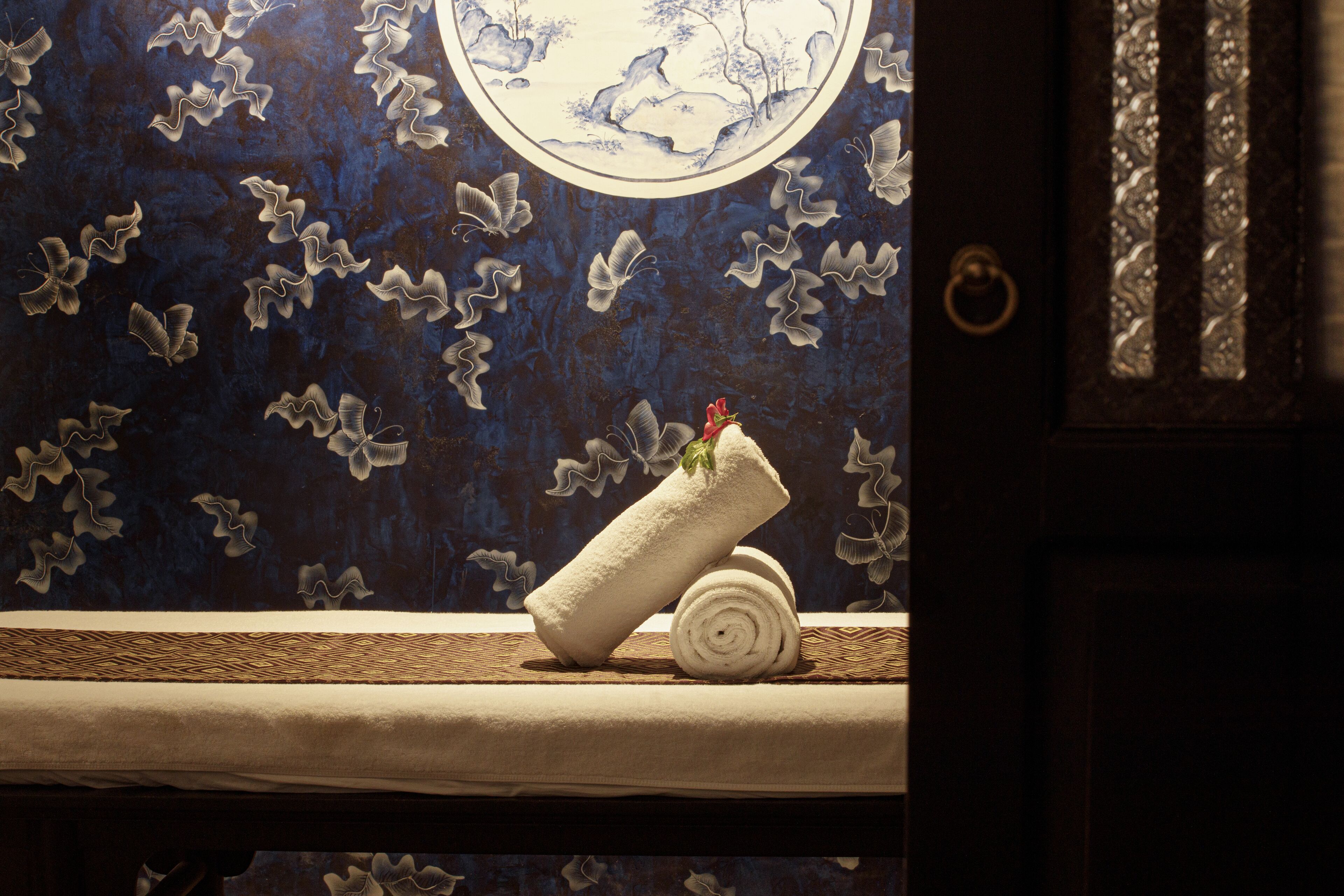 Un baño con una toalla sobre una repisa, un detalle decorativo en la pared con un diseño circular, y una puerta con pomo.