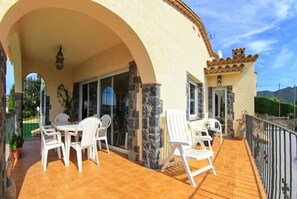 A covered patio with white chairs and a table, stone pillars, and a view of the surrounding landscape. - Club Villamar - Cozy villa with saltwater pool and panoramic views (Calonge)