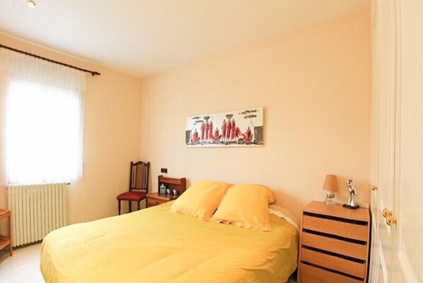 A bedroom with a bed, a nightstand, a chair, and a radiator. - Club Villamar - Cozy villa with saltwater pool and panoramic views (Calonge)