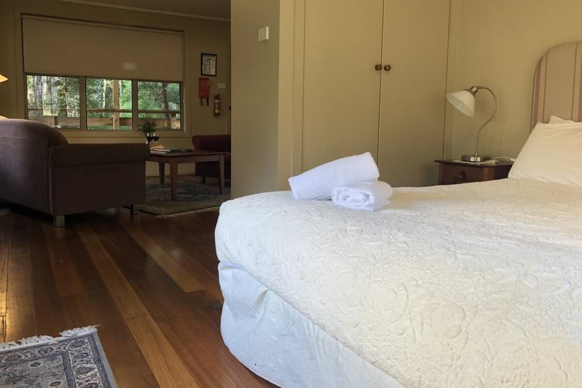 A hotel room with a large bed, a desk, a chair, and a window with a view of trees.