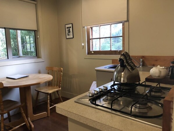 A kitchen with a gas stove, wooden chairs, a table, and a window. - Corinna Wilderness Village (Corinna)