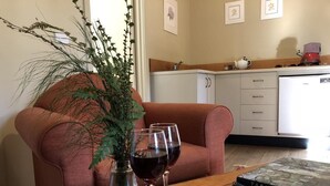 A cozy living room with a sofa, a table with a book, glasses of red wine, and a vase with greenery. - Corinna Wilderness Village (Corinna)