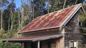 A rustic wooden cabin with a metal roof, a porch with green chairs, and a small window. - Corinna Wilderness Village (Corinna)
