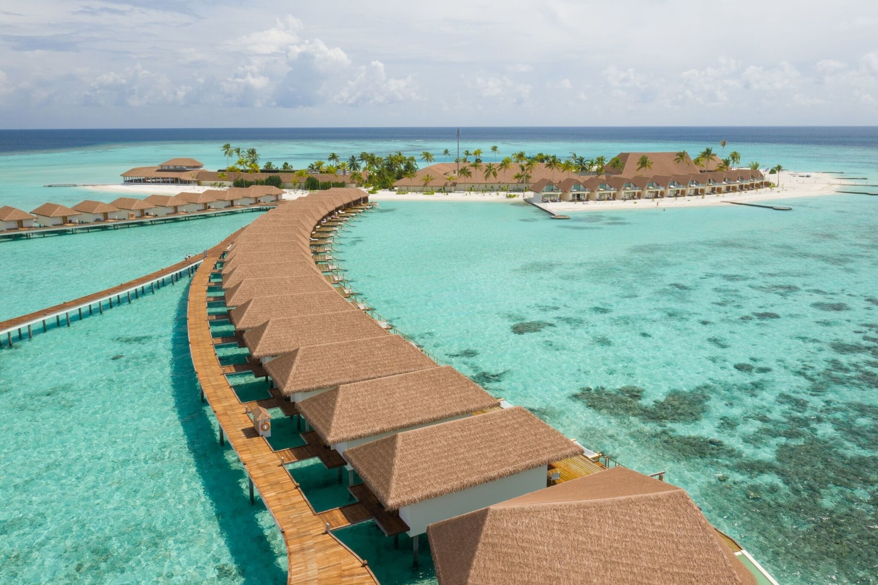 Overwater bungalows met rieten daken en houten steigers die uitsteken in turkoois water.