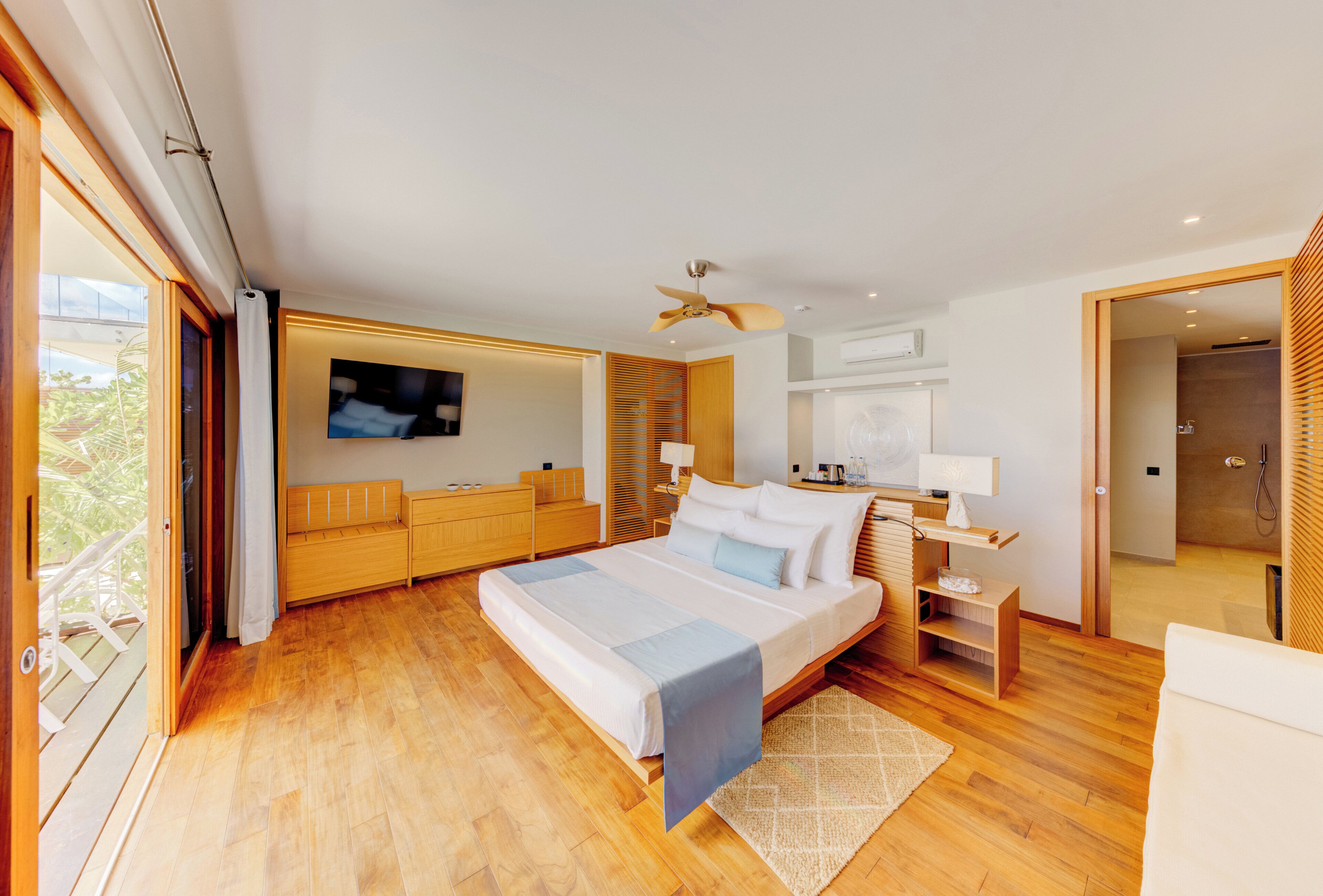 Ein modernes Schlafzimmer mit einem großen Bett, Holzböden, einem Deckenventilator, einem Fernseher und einem Balkon.