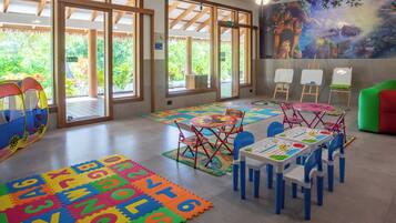 A children's playroom with colorful alphabet foam mats, tables with chairs, and a mural on the wall.