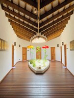 Un pasillo espacioso con suelo de madera, un macetero central con plantas y un techo con vigas a la vista.