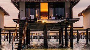 An overwater bungalow with a thatched roof, a staircase leading to the upper level, and a view of the water below. - Cinnamon Velifushi Maldives (Aarah)