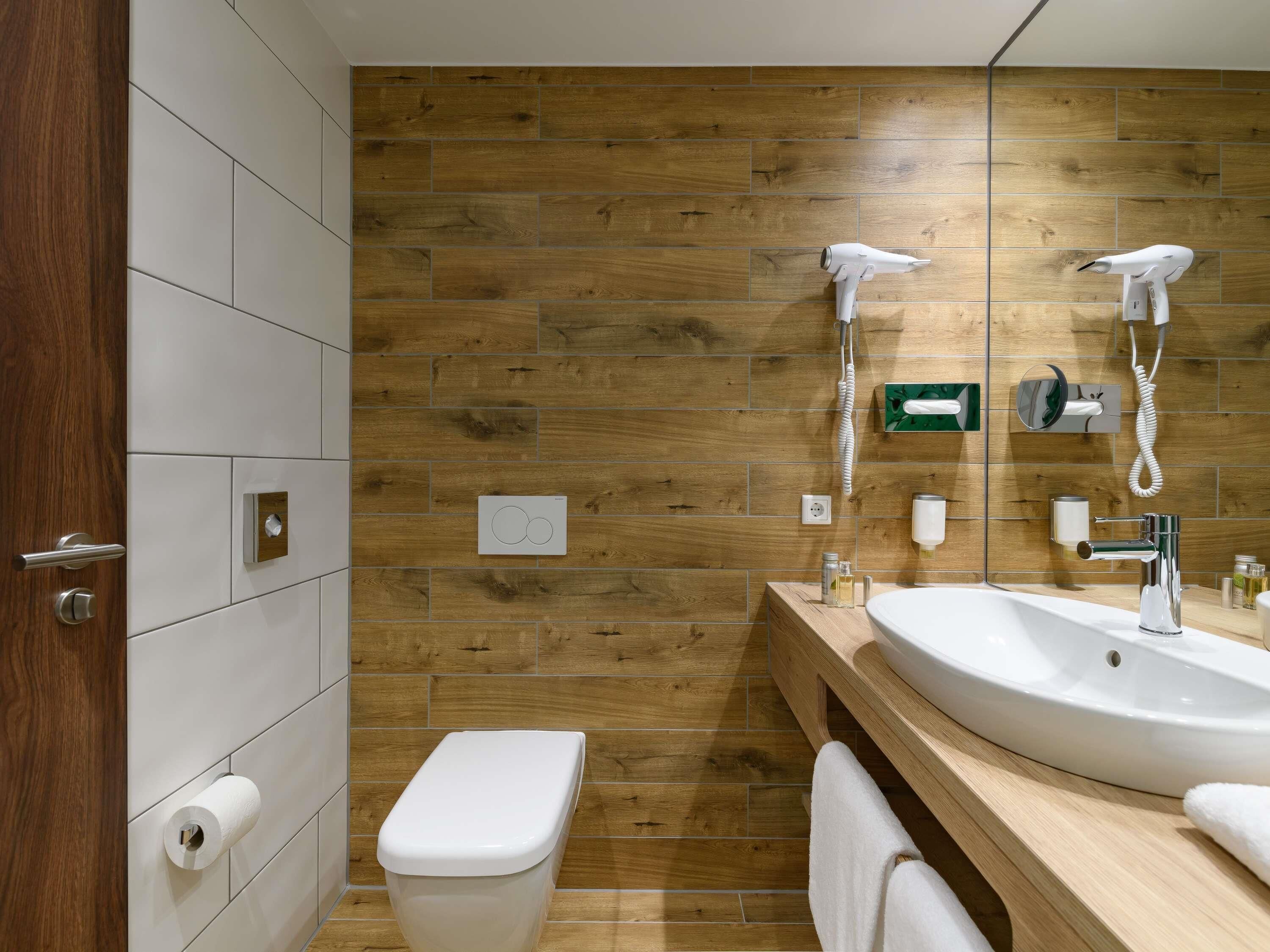 Une salle de bain moderne avec un mur en bois, des toilettes blanches, un lavabo avec un miroir et un sèche-cheveux.