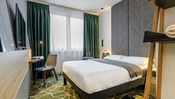 A hotel room with a bed, a desk, a chair, a TV, and a window with curtains.