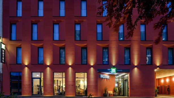 Un hôtel moderne, avec une façade rouge, de nombreuses fenêtres et une entrée bien visible, agrémentée d’une enseigne.