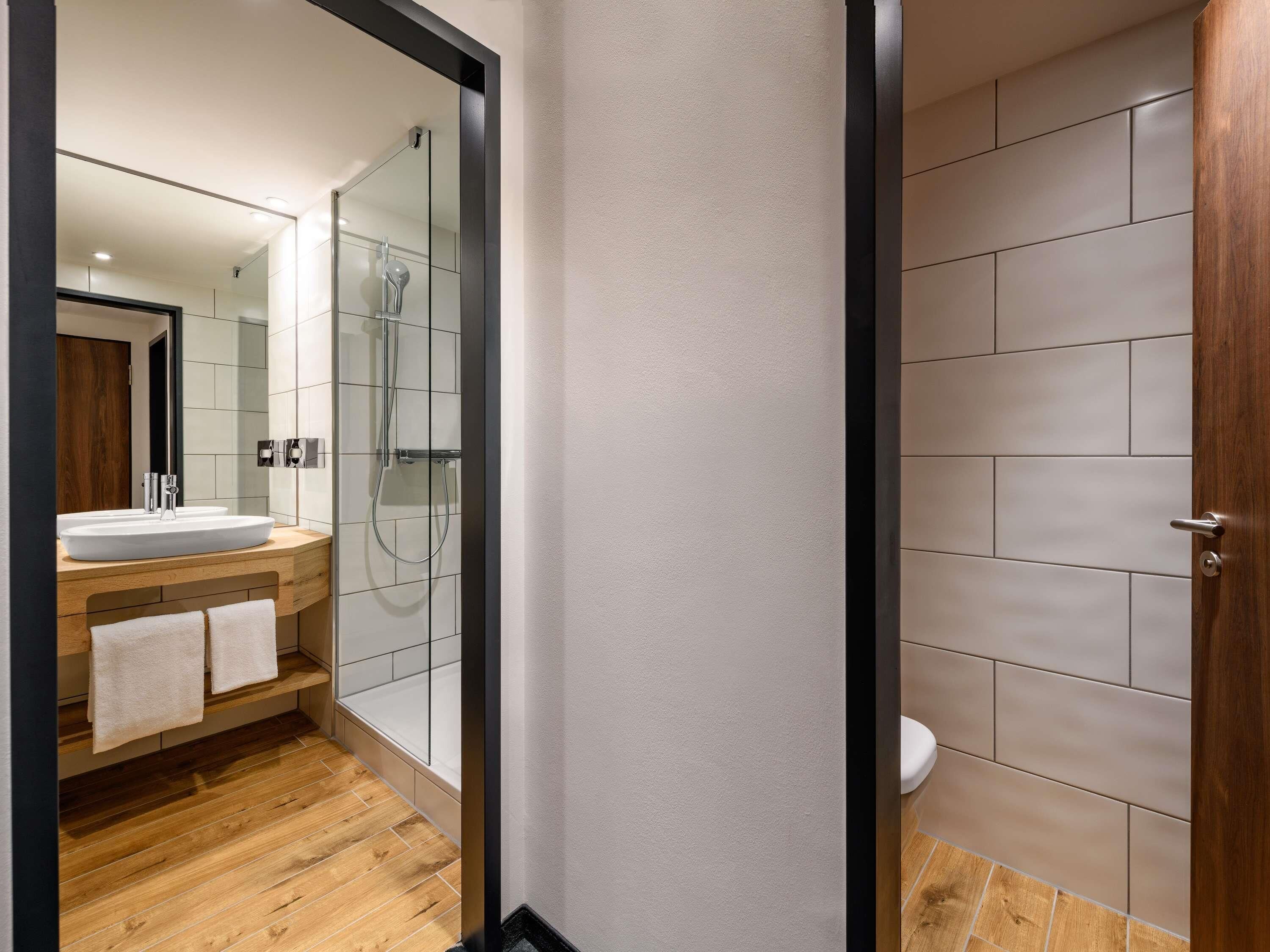 A modern bathroom with a large mirror, a wooden vanity, a glass shower enclosure, and a toilet.