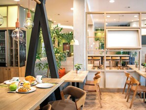 L’intérieur d’un café moderne, avec des tables et des chaises en bois, des luminaires suspendus et des plantes d’intérieur.