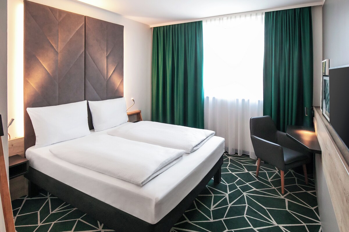 A hotel room with a double bed, a desk, and a chair.