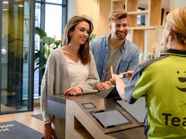 Ein Empfangsbereich mit digitalem Check-in, Holzausstattung und Glastür.
