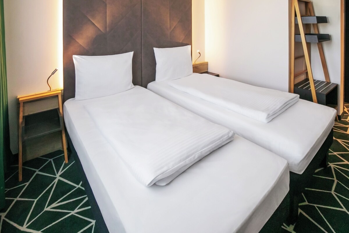 A hotel room with two single beds, a wooden headboard, a bedside table, and a patterned carpet.