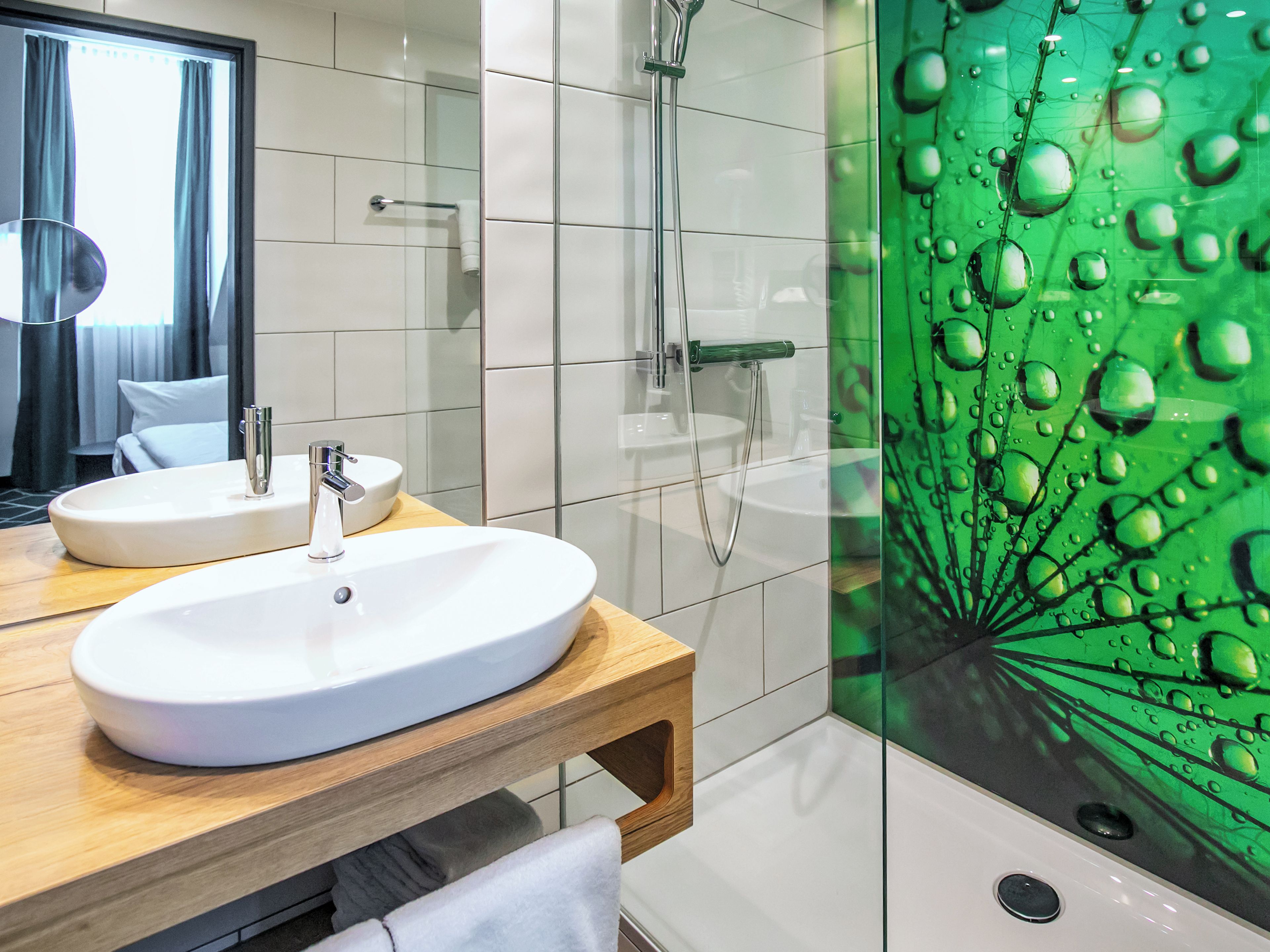 A bathroom with two sinks, a shower, and a glass partition with water droplets.
