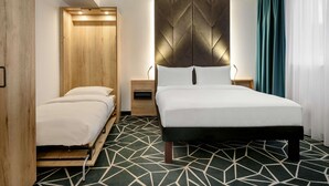 Une chambre d’hôtel moderne, équipée d’un lit, d’une armoire en bois, d’une table de chevet et d’un tapis à motifs géométriques.