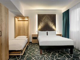 Ein modernes Hotelzimmer mit einem Bett, einem Holzschrank, einem Nachttisch und einem Teppich mit geometrischem Muster.