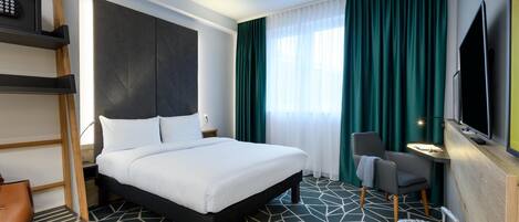 Habitación de hotel con cama, escritorio, silla, televisor y maleta.