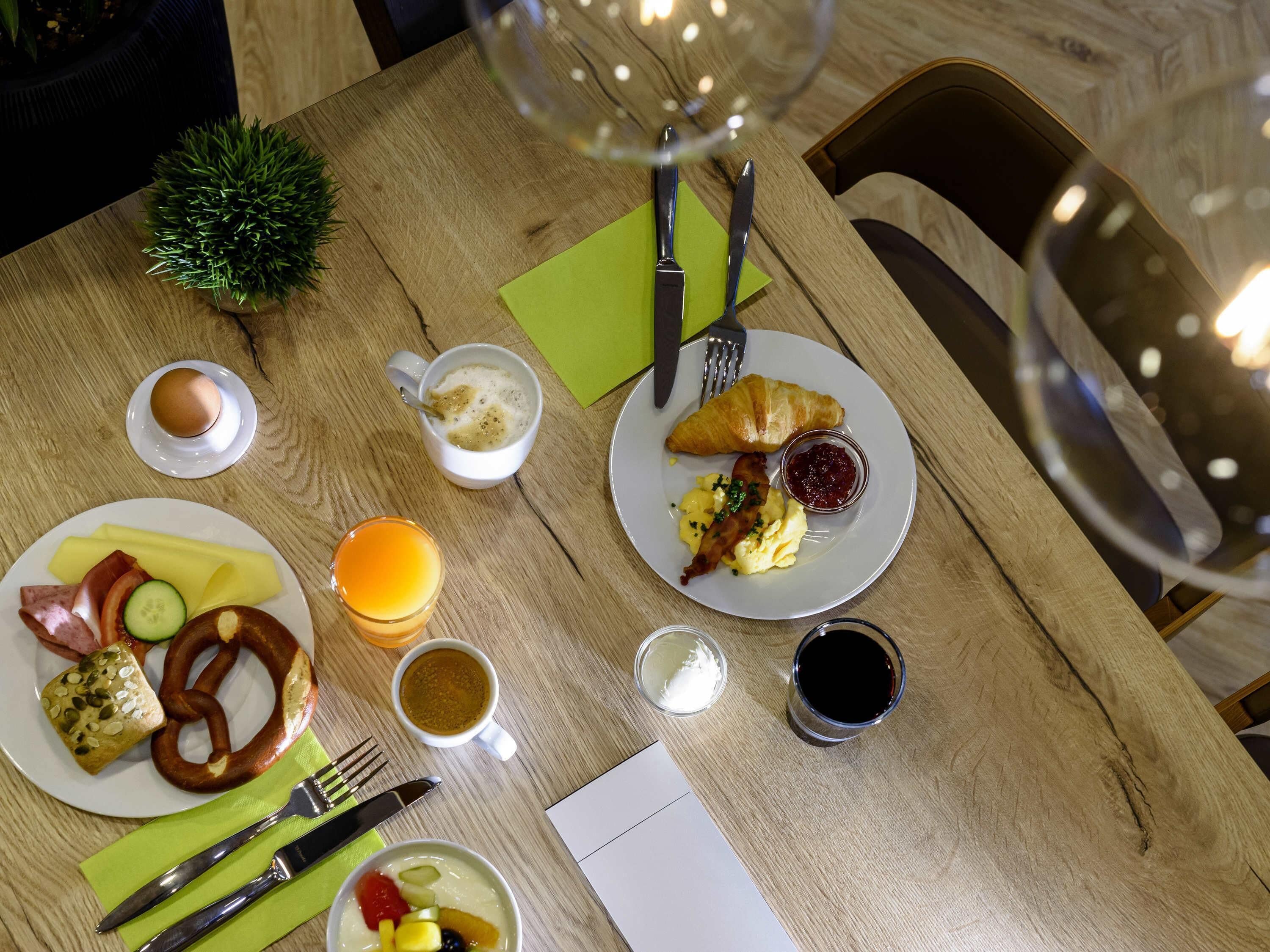 A wooden table with breakfast items, including eggs, bacon, a croissant, and a glass of orange juice.