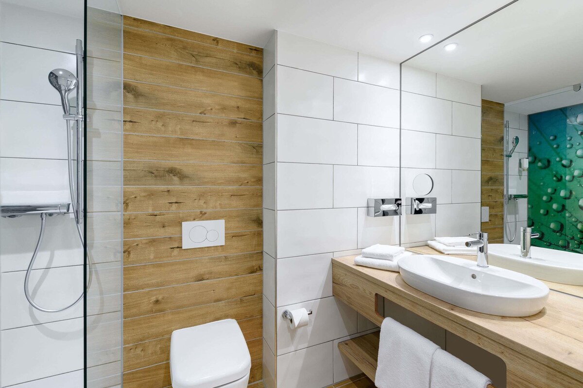 A modern bathroom with a wooden accent wall, a white toilet, a sink with a mirror, and a shower area.