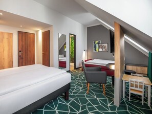 Une chambre d’hôtel comprenant un lit, un bureau, une chaise, une petite table, un miroir et un escalier menant à un étage supérieur.