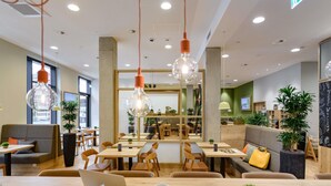 Un café moderne avec des tables et des chaises en bois, des luminaires suspendus et des plantes en pot.