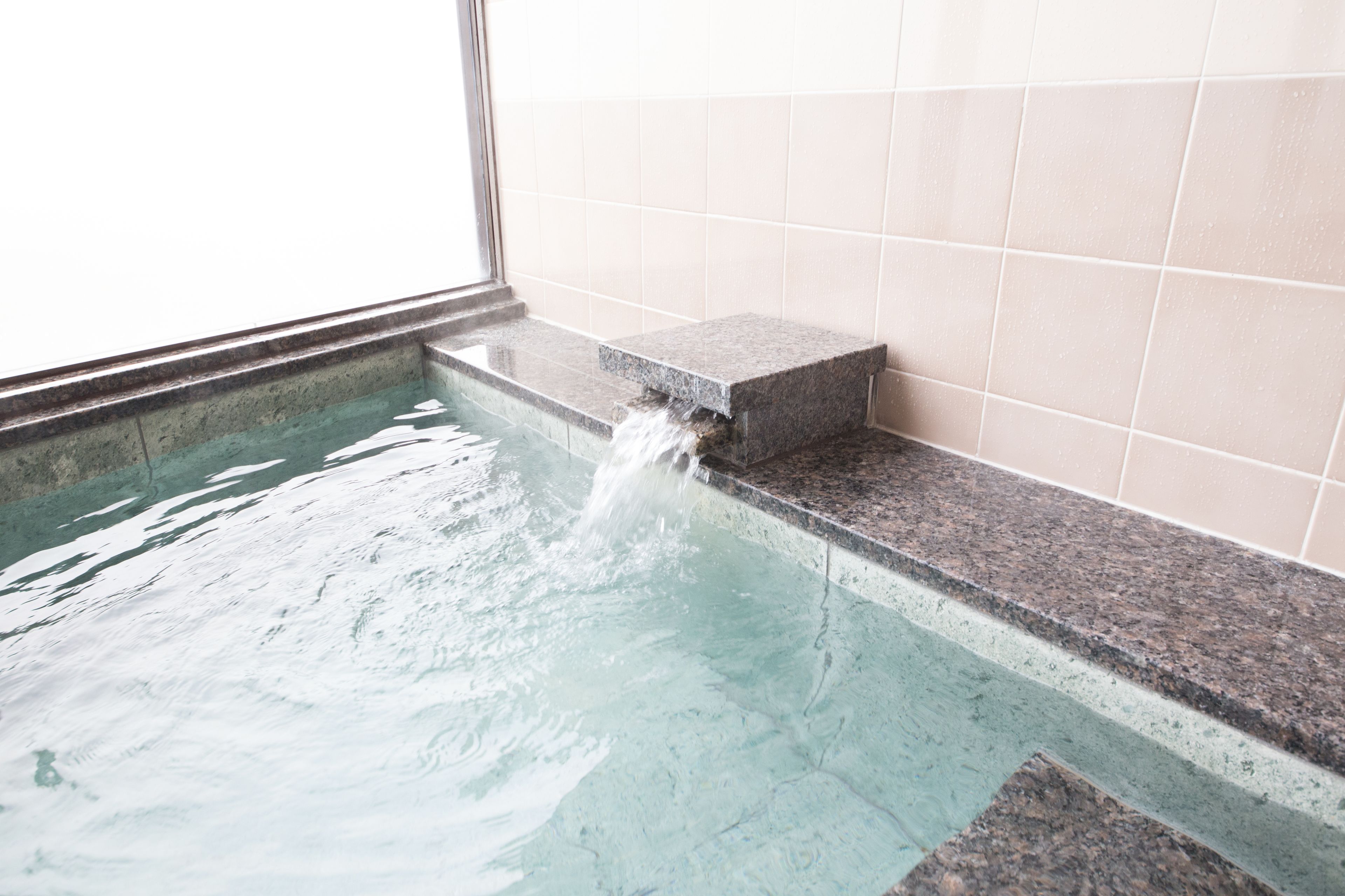 Une petite piscine intérieure agrémentée d’un élément décoratif aquatique, avec des murs carrelés et une fenêtre.