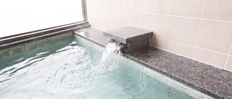 A small indoor pool with a water feature, tiled walls, and a window.