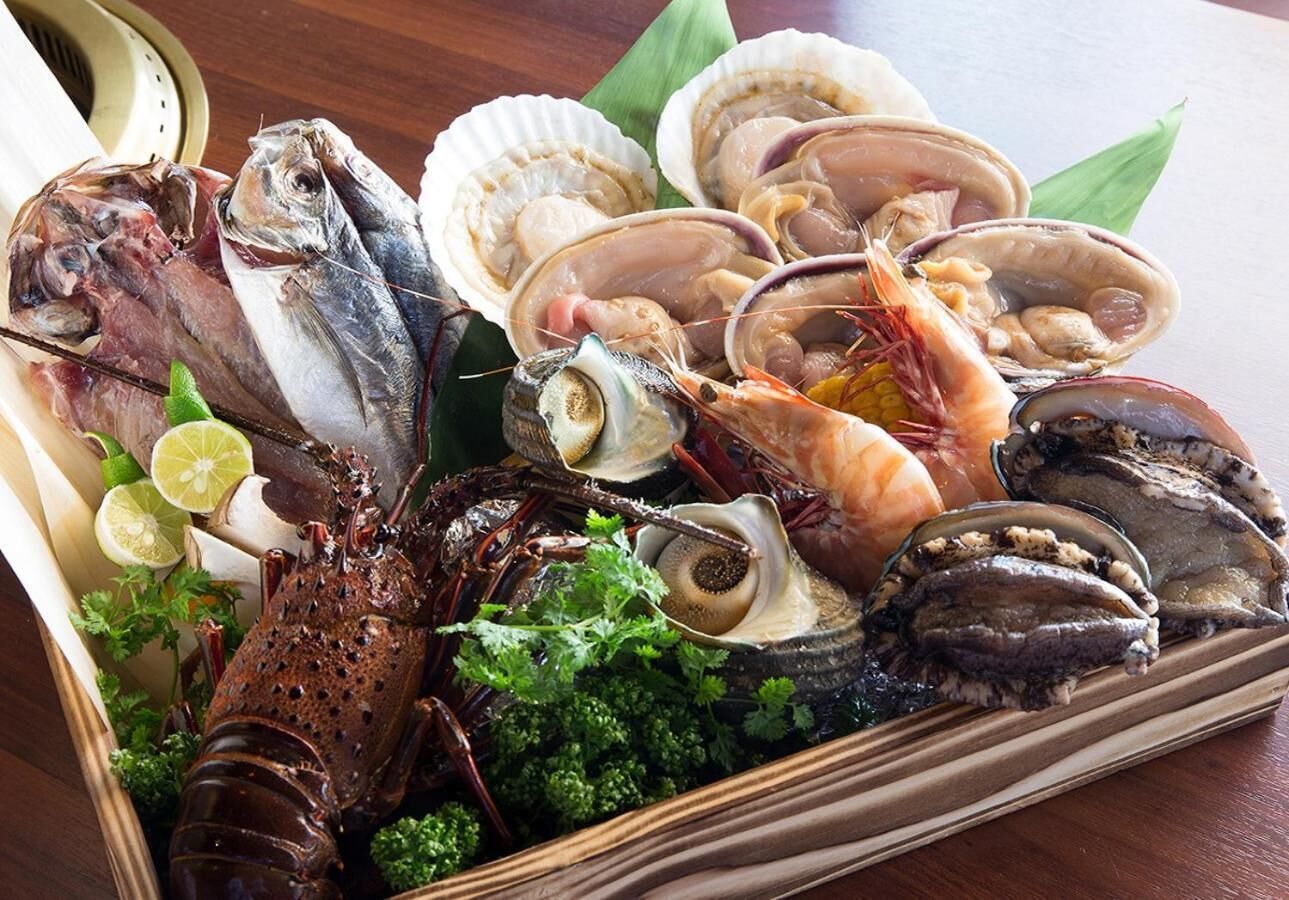 Variedad de mariscos, incluyendo pescado, camarones y almejas, dispuestos en una bandeja de madera junto con lima y perejil.