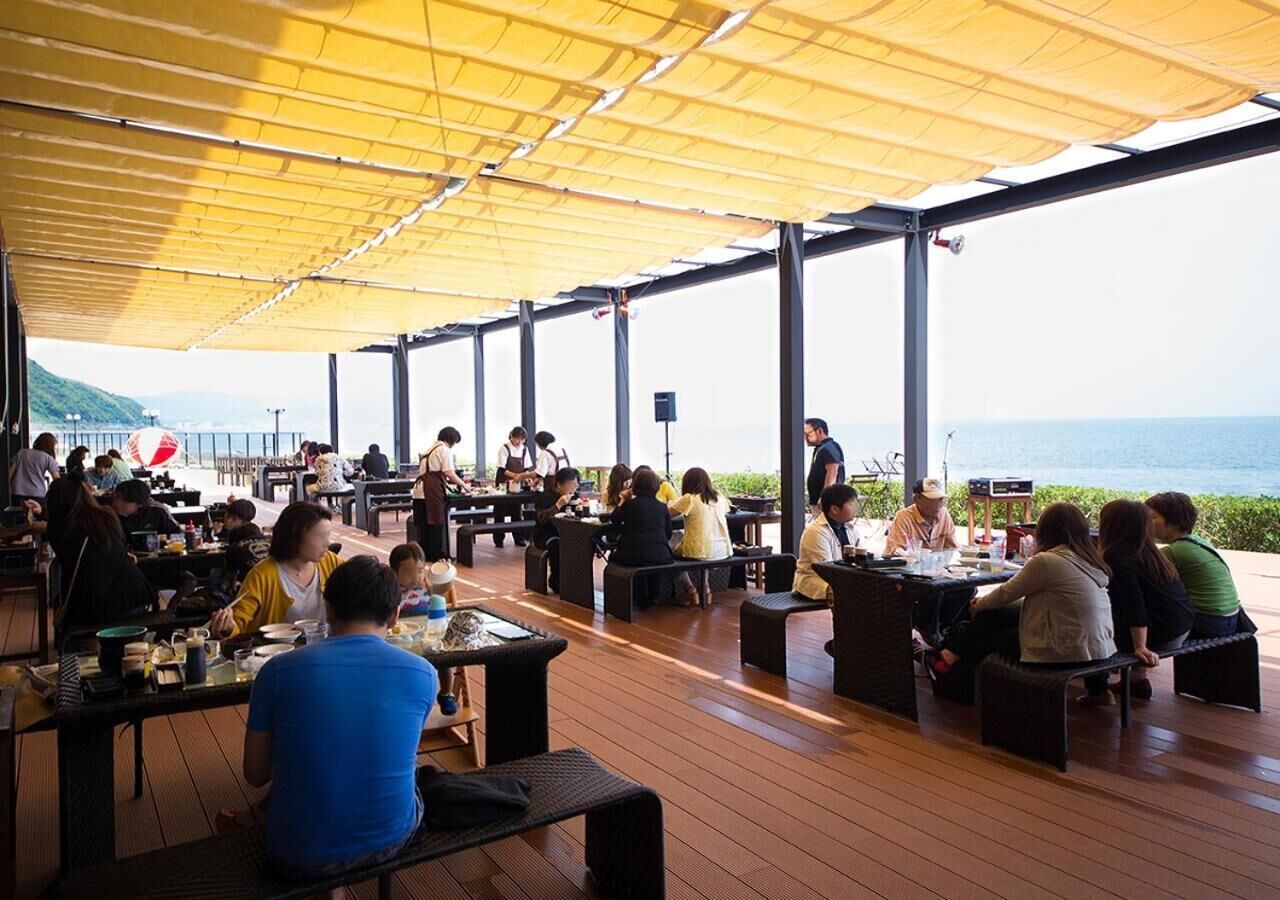 An outdoor dining area with tables and chairs, a covered section, and a view of the sea.