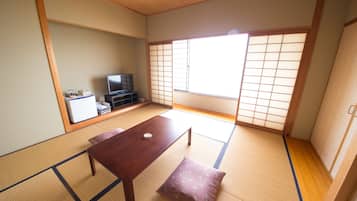 A traditional Japanese room with tatami flooring, a low wooden table, a bench, a television, and sliding doors.