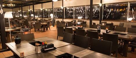 A restaurant with multiple tables and chairs, a high ceiling with exposed beams, and pendant lighting.