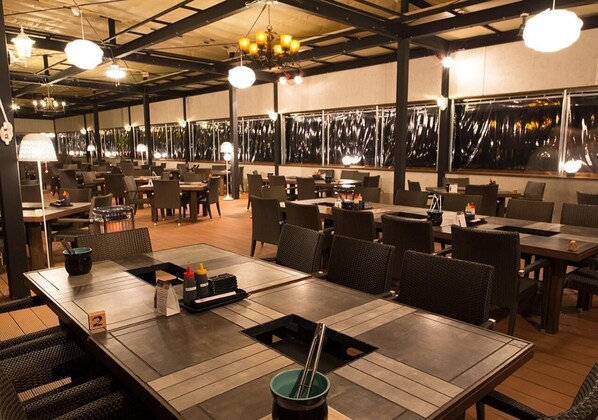 A restaurant with multiple tables and chairs, a high ceiling with exposed beams, and pendant lighting. - Sea Aiga Kaigetsu (Sumoto)