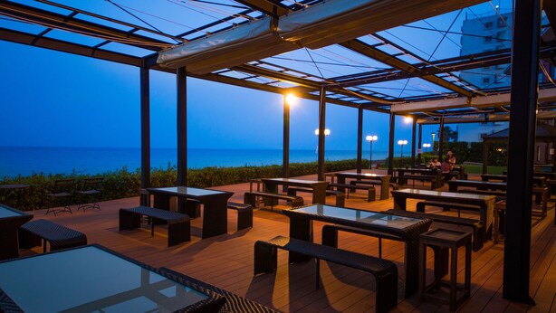 An outdoor dining area with tables and chairs, a glass-top table, and a view of the sea. - Sea Aiga Kaigetsu (Sumoto)