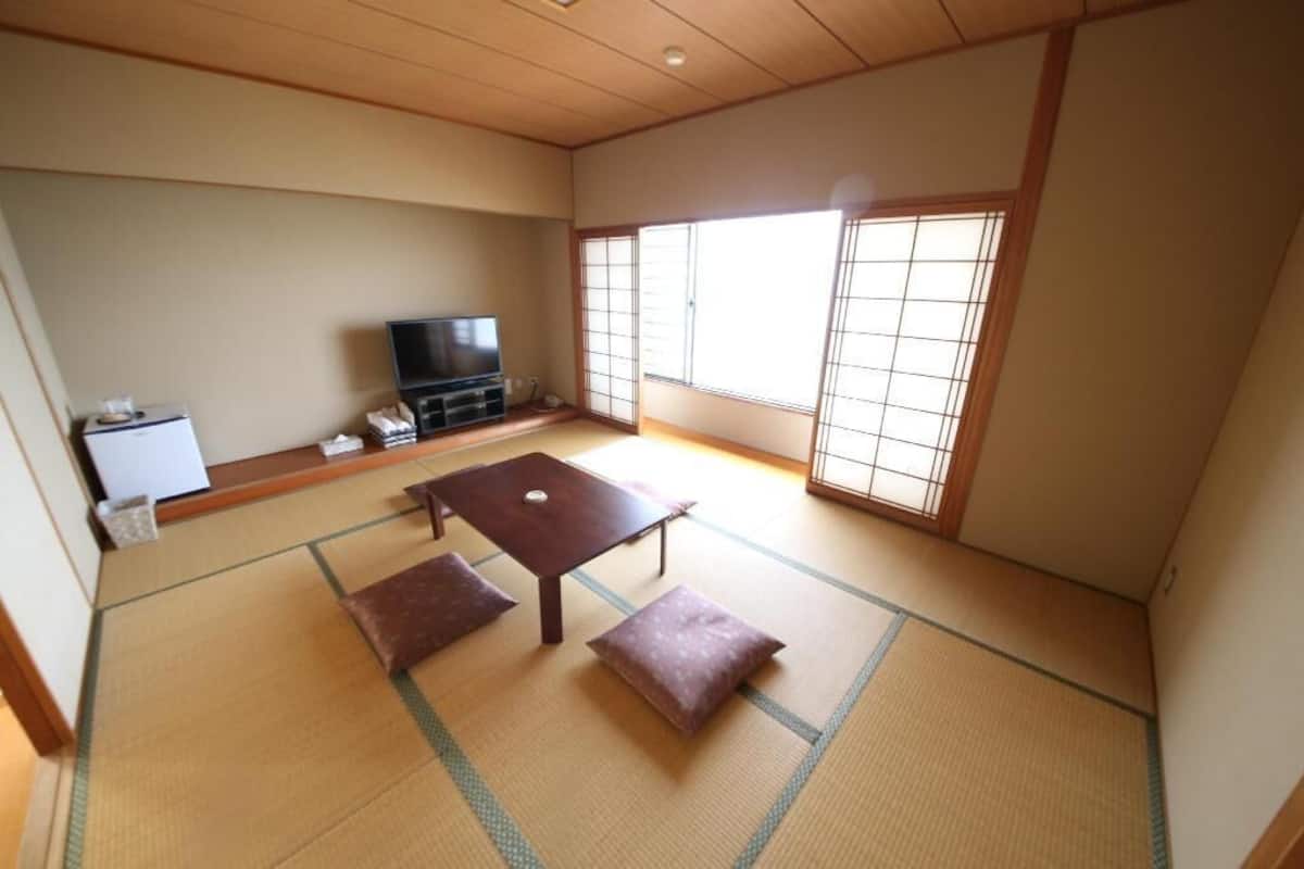 A traditional Japanese room with tatami flooring, a low table with cushions, a television, and sliding shoji doors.