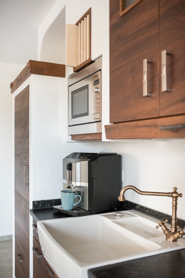 Una cocina moderna con microondas integrado, cafetera y un lavamanos con grifo de estilo vintage.