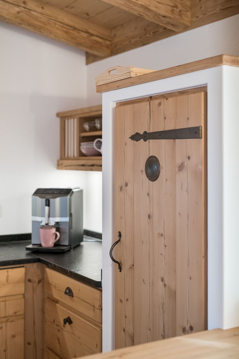 A wooden door with a black handle and a metal plate, a coffee maker on the counter, and wooden cabinets.