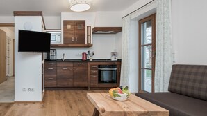 Une cuisine moderne avec des meubles en bois, un four à micro-ondes encastré et un coin repas comprenant une table en bois et un saladier rempli de fruits.