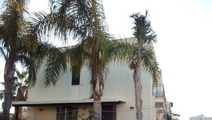 Ein Wohngebäude mit einer beigen Fassade, Palmen und einem verschlossenen Eingang.