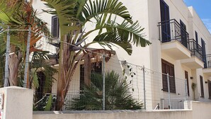 Ein modernes Gebäude mit weißer Fassade, mehreren Balkonen und einem Eingangsbereich mit bepflanztem Tor.