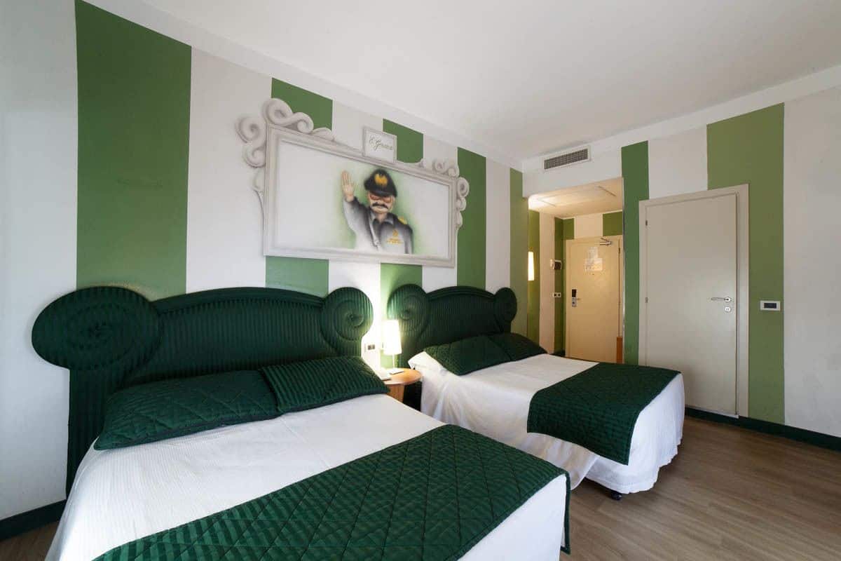 A hotel room with two beds, green and white bedding, a framed picture on the wall, and a door to another room.